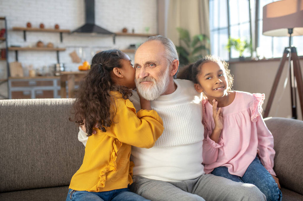 Cute long-haired girl telling something on the ear to her granddad - Φωτογραφία, εικόνα