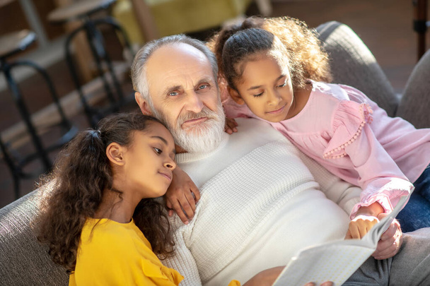 Grey-haired granddad reading a book to his granddaughters - Foto, afbeelding