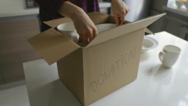 donate household items - woman putting tableware in cardboard box for donation on kitchen table - Footage, Video