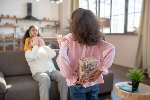 Dark-skinned girl in a pink shirt hiding a birthday gift for her grandfather behind her back - Foto, Bild