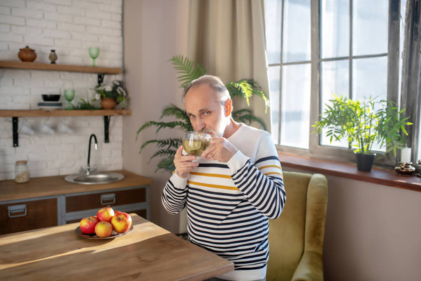 Bearded grey-haired man in a striped sweater having tea at home - Foto, Imagem