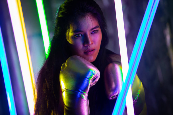 Schöne Asiatin trainiert und boxt mit silbernen Handschuhen. Office Girl Übungen in moderner Farbe Neon Muay Thai Boxen Gym mit Schweißwasserspritzer - Foto, Bild
