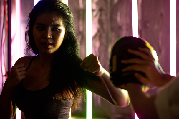 Красиві 20-ті азіатські жінки тренуються бити з тренером на Срібному золоті Міттс-Ґловс. Офіс Дівчата на Modern multi color Fashion Neon Muay Thai Boxing Gym з потоком води. - Фото, зображення
