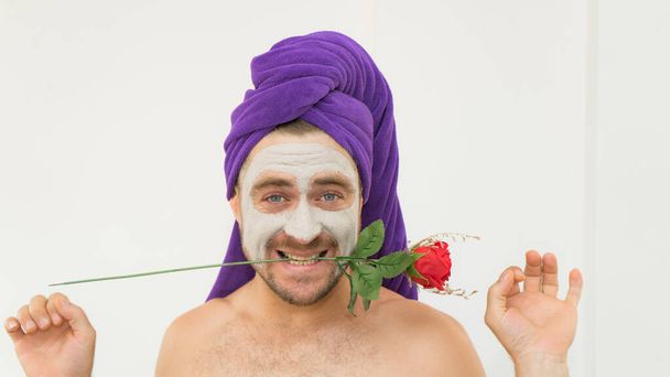 Emotional handsome funny man holding rose in his teeth wearing bath cap and cosmetic mask in his face. Funny crazy man wih rose  for Women day concept .Man copies woman behaviour in comical way. - Photo, Image