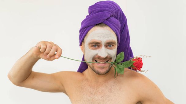 Emotional handsome funny man holding rose in his teeth wearing bath cap and cosmetic mask in his face. Funny crazy man wih rose  for Women day concept .Man copies woman behaviour in comical way. - Fotografie, Obrázek