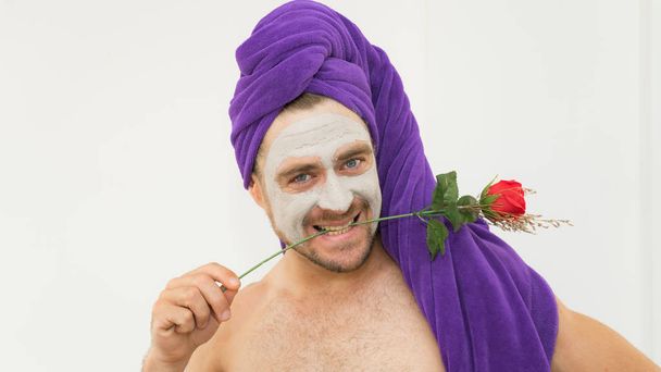 Emotional handsome funny man holding rose in his teeth wearing bath cap and cosmetic mask in his face. Funny crazy man wih rose  for Women day concept .Man copies woman behaviour in comical way. - Foto, imagen