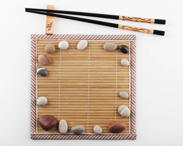 Palillos se encuentran en un soporte junto a una estera de bambú, en la superficie de la que se colocan piedras decorativas alrededor
 - Foto, imagen