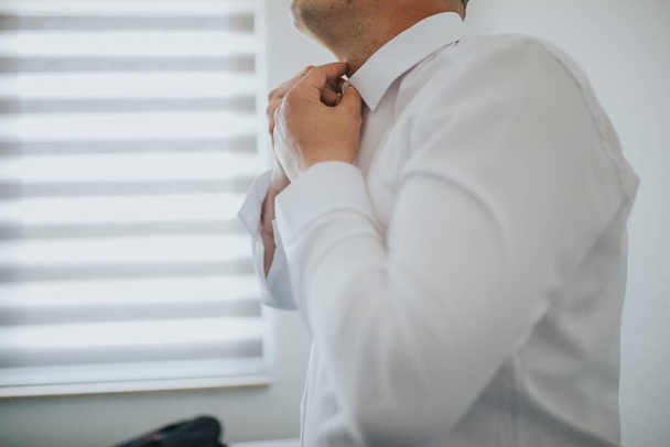A closeup shot of a male fastening a button of a white shirt - 写真・画像