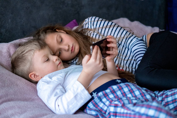 Two kids caucasian boy and girl playing games or looking information video text at Internet on mobile phones at home lying in bed. Digital technology, Modern childhood  - Foto, immagini