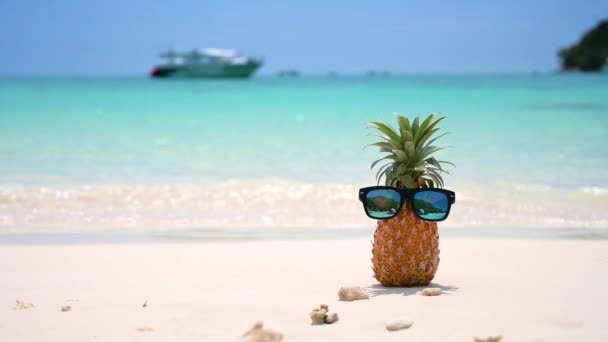 Bicchieri ananas si trovano sulla spiaggia in riva al mare al sole caldo, ponendo il concetto per l'estate
. - Filmati, video