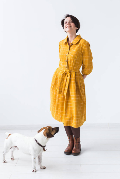 Cheerful young woman posing in a yellow dress with her beloved dog Jack Russell Terrier standing on a white background. The concept of casual wear and pets - Foto, Bild
