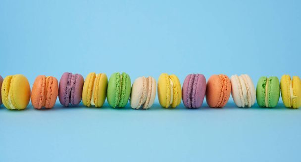 many multi-colored round baked macarons cakes on a light blue background, dessert stands in a row - 写真・画像