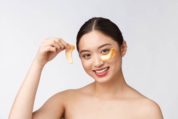 Asyalı güzel bir genç kadın, gözlerinin altında altın maskelerle cildini önemser. - Fotoğraf, Görsel