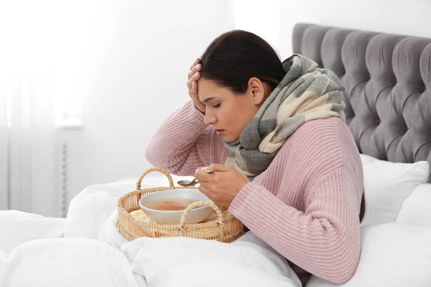 Sick young woman eating soup to cure flu in bed at home - Foto, afbeelding