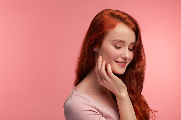 Portrait of smiling redhead girl. Perfect skin. Beautiful female model with long hair over pink background. Young cute woman with clear skin. Skincare and facial treatment concept - Фото, изображение