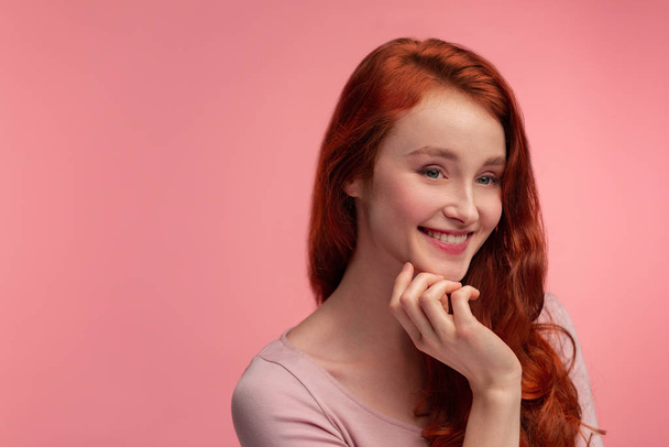 Portrait of smiling redhead girl. Perfect skin. Beautiful female model with long hair over pink background. Young cute woman with clear skin. Skincare and facial treatment concept - Photo, image