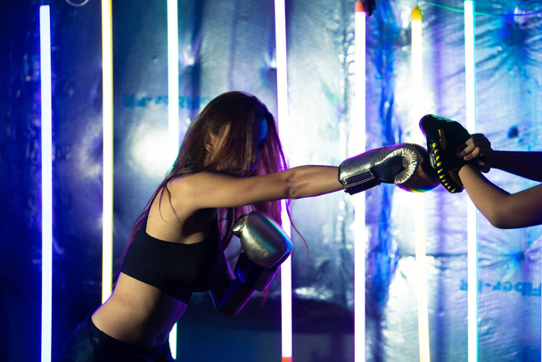 Прекрасні 20-ті азіатські жіночі трансгендерні потяги б'ються з тренером на Срібному золоті Міттс-Гловс. Офіс Дівчата на Modern multi color Fashion Neon Muay Thai Boxing Gym з потоком води. - Фото, зображення