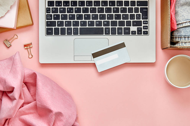 ノートパソコン、クレジットカード、小包や服をピンクの机のテーブルの上にオンラインショッピングのコンセプト。トップ表示. - 写真・画像