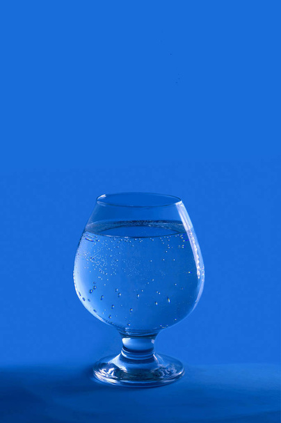 Mavi arka planda bir bardak temiz soğuk su. İçme suyu. Monokrom görüntüsü. Asgari renk konsepti. Dikey resim, boşluğu kopyala - Fotoğraf, Görsel