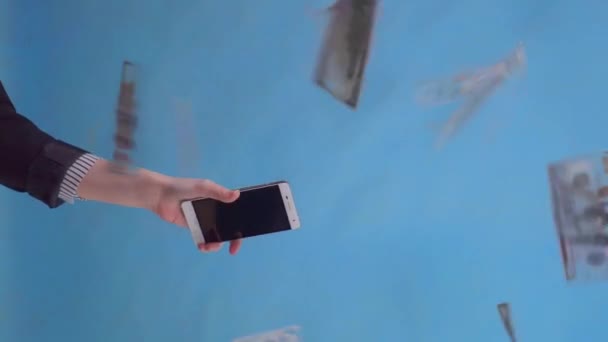 hand holding a smartphone against the background of falling banknotes isolate - Video