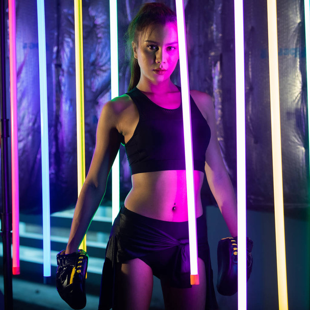 Beautiful Asian Woman Transgender is training and punching with Silver gold Mitts Gloves. Office Girl strong stand between Modern color Neon Muay Thai Boxing Gym with sweat water splash - Photo, Image