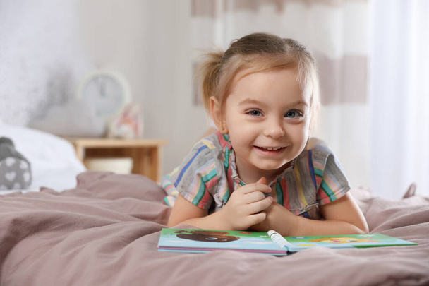 Cute little girl with book on bed at home - Foto, Imagem