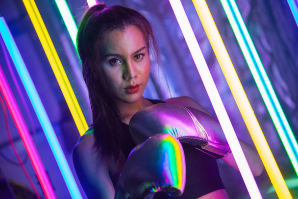 Beautiful 20s Asian Woman punch, poses with Silver gold Mitts Gloves. Office Girl exercise between Modern multi color Fashion Neon Muay Thai Boxing Gym with sweat water splash - Foto, Imagem