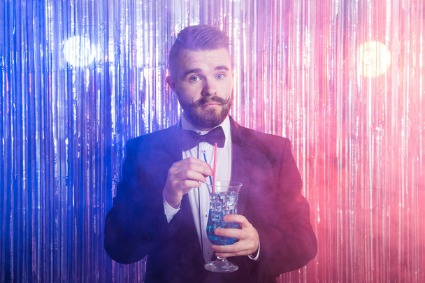 Klubová párty a dovolená koncept - Portrét elegantního pohledného muže v drahém obleku drží modrý koktejl na lesklém pozadí. - Fotografie, Obrázek