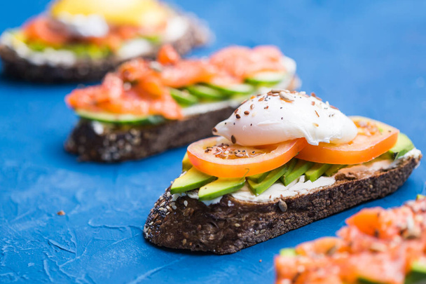 Sandwiches con salmón ahumado, huevos, salsa y aguacate sobre fondo azul. Concepto de desayuno y nutrición saludable
. - Foto, imagen