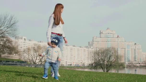 Little baby boy and his young mother walking to the camera on the spring city background and reaching the camera the baby smiles in it in 4K medium shot video. - Séquence, vidéo