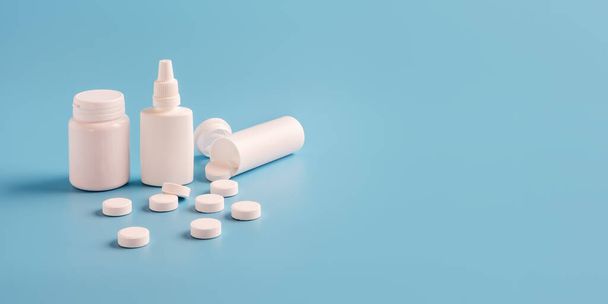 ラベルなしの錠剤と青い背景の散乱錠剤のための3つの白いプラスチック製の薬瓶。テキストまたは広告のコピースペース - 写真・画像