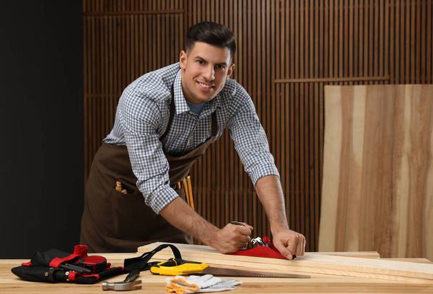 Handsome carpenter working with timber at table indoors - Фото, зображення