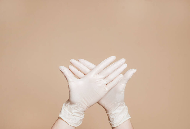Two hands wearing white gloves on brown background. Stop the virus. Conceptual photo. - Фото, изображение
