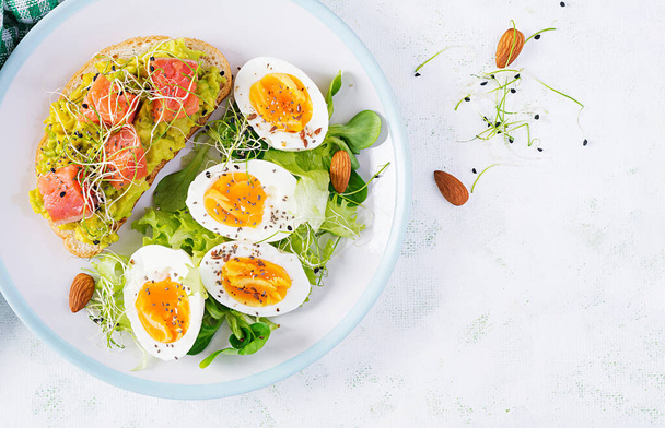 Kahvaltıda. Avokado ve somonlu sağlıklı bir sandviç haşlanmış yumurta, otlar, fotokopi alanı olan beyaz tabakta chia tohumları. Sağlıklı protein yiyeceği. Üst görünüm, genel görünüm - Fotoğraf, Görsel