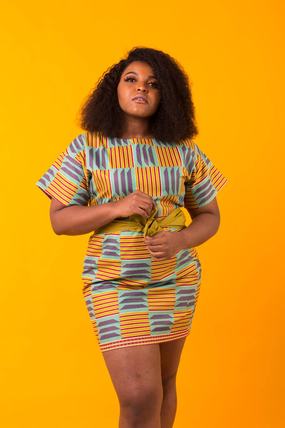 Young beautiful african american girl with an afro hairstyle. Portrait on yellow background. Girl looking at camera. - Fotó, kép