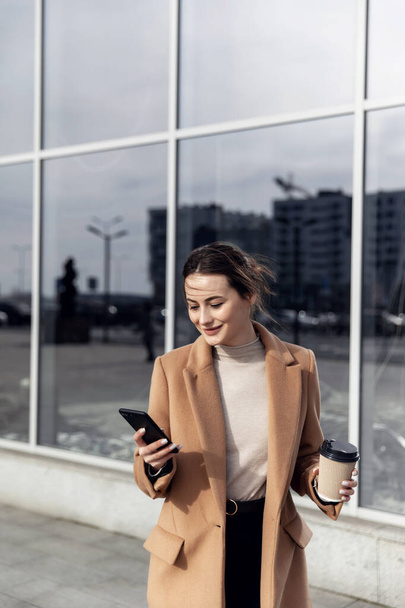 Business Woman smiling charmingly, using her Smartphone. Female enjoying sunny day and funny conversation. Typing on her Phone with Interest. Brunette Girl. Successful Woman. Phones. Apps. - Foto, Bild