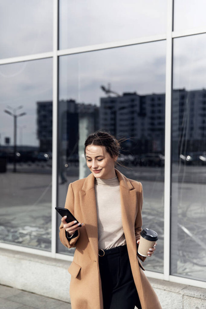 Business Woman smiling charmingly, using her Smartphone. Female enjoying sunny day and funny conversation. Typing on her Phone with Interest. Brunette Girl. Successful Woman. Phones. Apps. - Foto, Imagen
