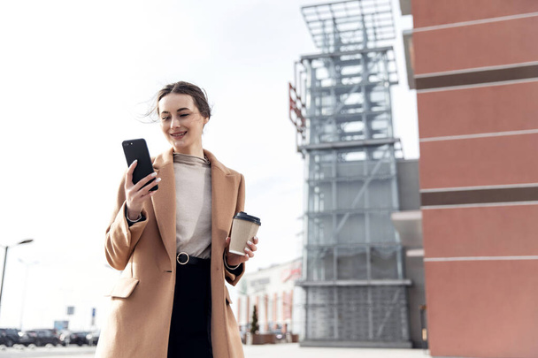 Business Woman smiling charmingly, using her Smartphone. Female enjoying sunny day and funny conversation. Typing on her Phone with Interest. Brunette Girl. Successful Woman. Phones. Apps. - Photo, Image