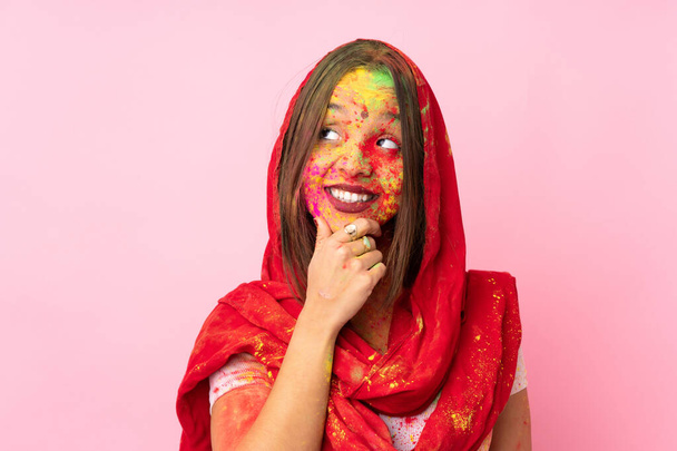Young Indian woman with colorful holi powders on her face isolated on pink background thinking an idea while looking up - Zdjęcie, obraz