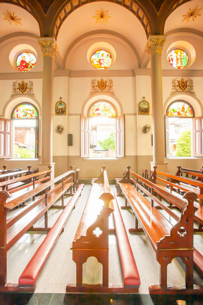 Ein beschauliches Kircheninterieur mit alten hölzernen Kirchenbänken, leuchtenden Sonnenstrahlen durch alte Fenster und Glasmalereien auf alten hölzernen Kirchenbänken, Santa Cruz Kirche oder Kudi Chin, Thailand. - Foto, Bild