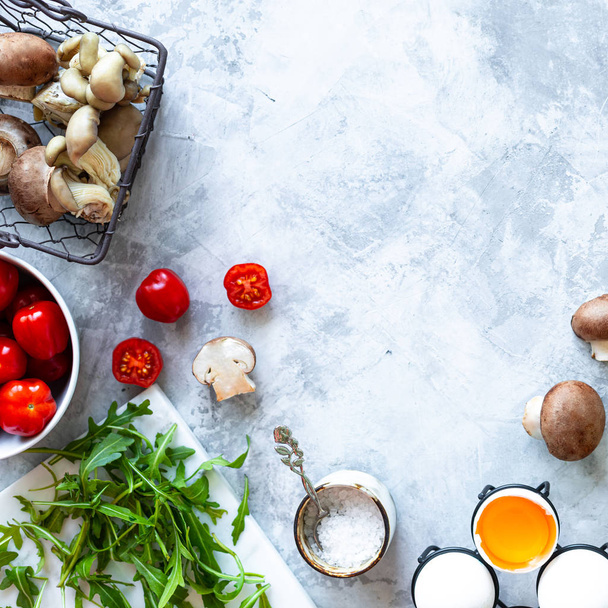 Ingrediënten voor het koken op een grijze betonnen achtergrond. Een bos verse groene asperges, eieren, spek, champignons, tomaten, arugula. Bovenaanzicht. Begrepen, ruimte. Vierkant - Foto, afbeelding