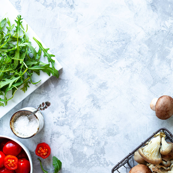 Ingredients for cooking on a gray concrete background. A bunch of fresh green asparagus, mushrooms, tomatoes, arugula. Top view. Copy space. Square - 写真・画像