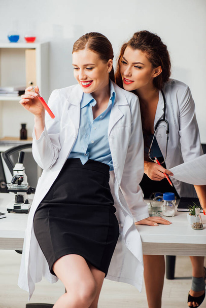 щасливі і сексуальні медсестри дивляться на пробірку з червоною рідиною в лабораторії
  - Фото, зображення
