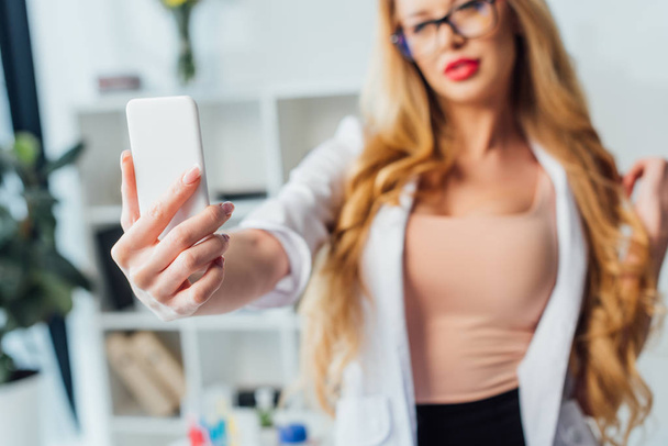 selective focus of sexy nurse in white coat taking selfie in clinic  - Foto, afbeelding