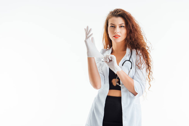 sexy nurse wearing latex gloves and looking at camera isolated on white  - 写真・画像