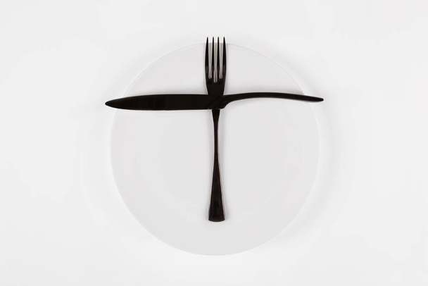 Langage de couverts, étiquette de salle à manger. Prêt pour le deuxième repas. Plaque ronde en céramique blanche avec couteau et fourchette isolés sur blanc, vue de dessus
 - Photo, image