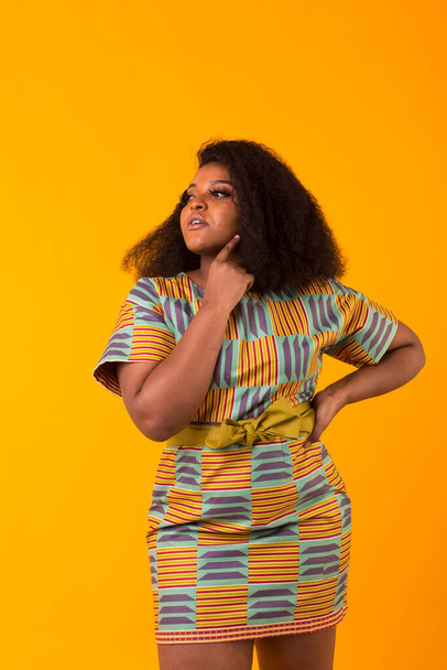 Young beautiful african american girl with an afro hairstyle. Portrait on yellow background. Girl looking at camera. - Foto, immagini