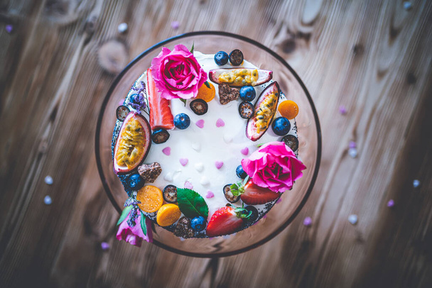 Taze meyveli tatlı beyaz cheesecake turtası ahşap masa arkasında haşhaş ve gül çiçekleri. Doğum günü, Sevgililer Günü ve kutlama için ideal bir hediye. - Fotoğraf, Görsel