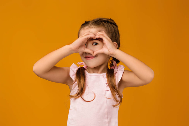Cute smiling little child girl making heart-shape gesture - Foto, imagen