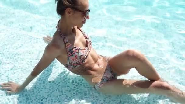 Νεαρή λεπτή σέξι γυναίκα μπικίνι χαλαρώνοντας στο νερό κάθεται στην πισίνα στο πολυτελές ξενοδοχείο spa - Πλάνα, βίντεο